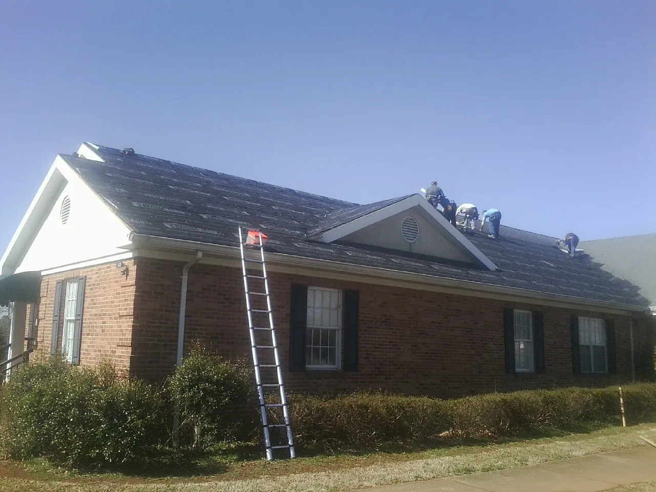 Crew tearing shingles off a brick ranch roof with a ladder set — Emergency Roof Repair work by our crew in Gibbstown