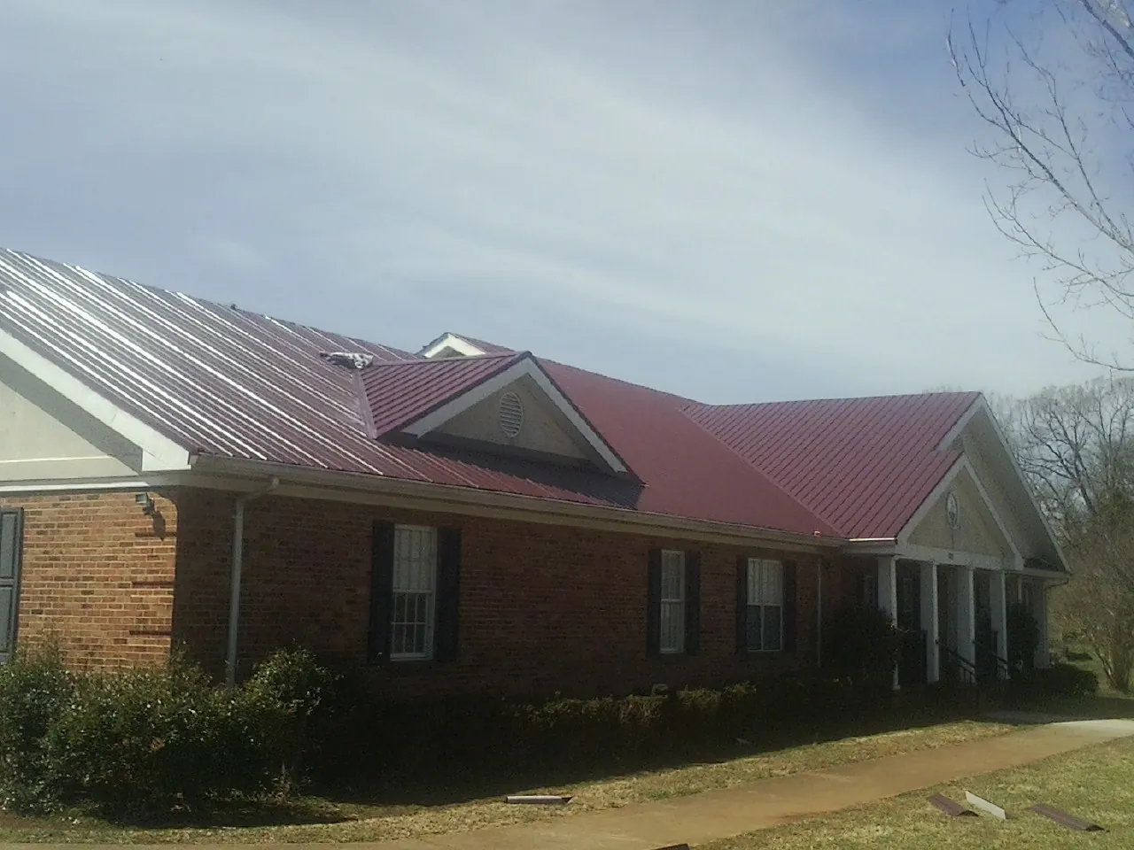 Red metal roof with gabled entries on a long brick building, from a Hail Damage Roof Repair job in Gibbstown