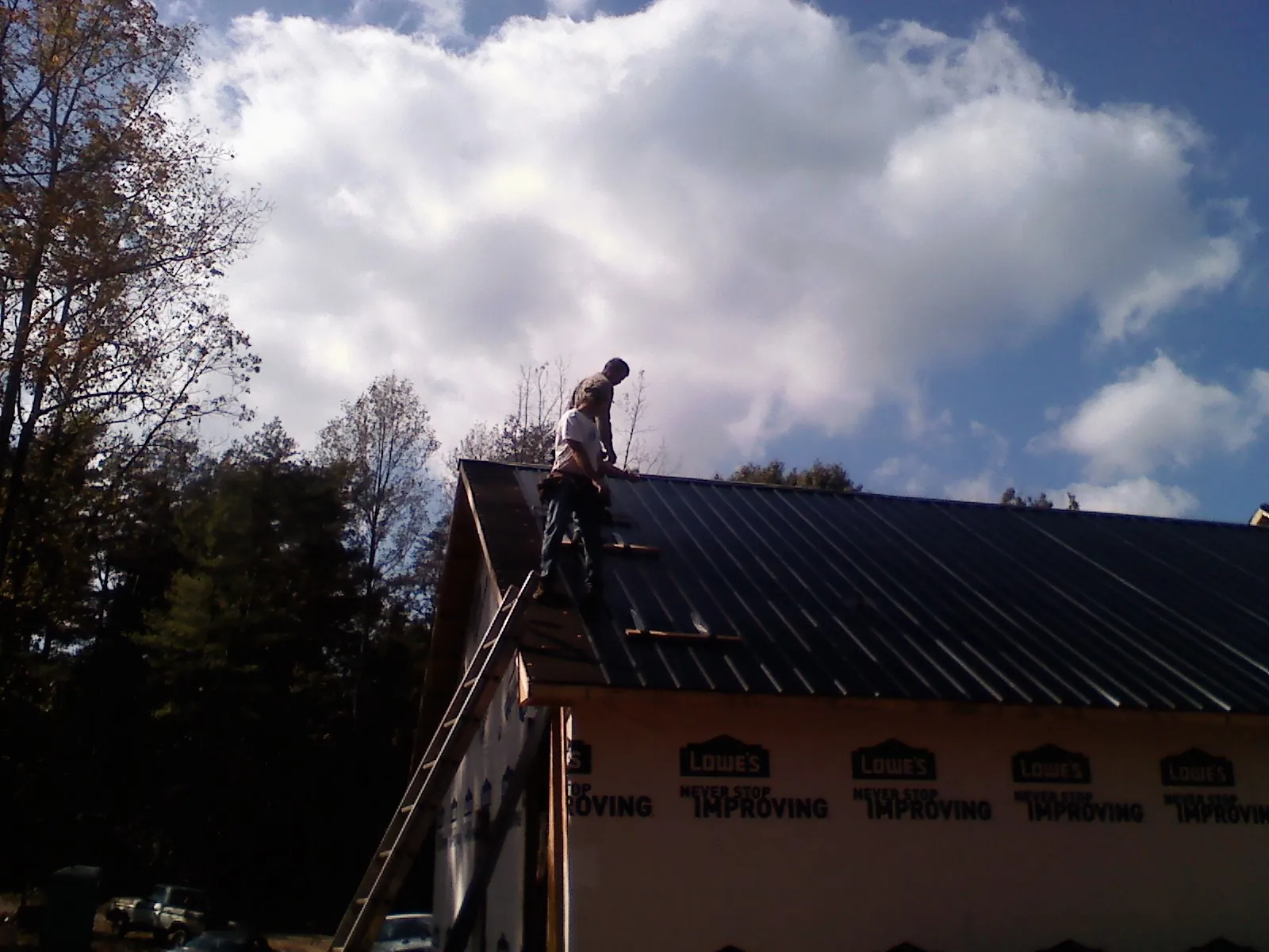 Roofer fastening dark metal panels high against a cloudy sky, from a Roof Inspection job in Gibbstown