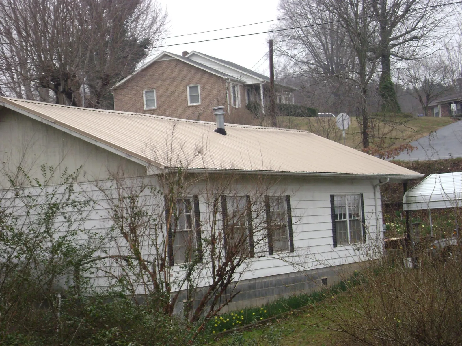 Tan metal roof on a white sided house set into a hillside — Commercial Roofing by Roofing Brothers in Gibbstown